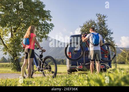 Ein junger Mann und eine Frau bereiten sich auf das Geländeradfahren vor und nehmen Elektro-Mountainbikes vom Fahrradträger im Wohnmobil ab. Stockfoto