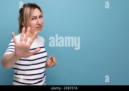 Trauriges blondes Mädchen, das ihre Hand auf blauem Hintergrund mit Kopierraum winkt Stockfoto