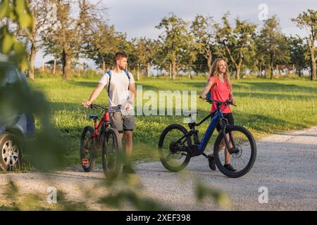 Ein junger Mann und eine Frau bereiten sich auf das Geländeradfahren vor und nehmen Elektro-Mountainbikes vom Fahrradträger im Wohnmobil ab. Stockfoto