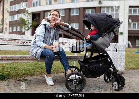 Glückliche junge Frau Eltern mit ihrem kleinen Sohn in einem Kinderwagen spazieren durch den Park und entspannen sich bei Kaffee Stockfoto