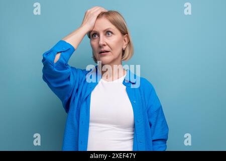 Überraschte blonde reife Frau in Unglauben auf blauem Hintergrund mit Copyspace Stockfoto