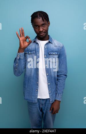 Porträt eines jungen, fröhlichen amerikaners mit Dreadlocks in einer Jeansjacke, die zeigt, dass alles in Ordnung ist Stockfoto