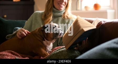Nahaufnahme Einer Frau Zu Hause Im Winter-Pullover, Die Buch Streichelt Haustier Französisch Bulldog Hund Liest Stockfoto