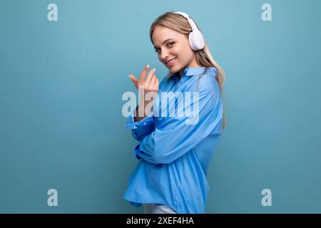 Nahaufnahme eines charmanten Mädchens in großen kabellosen Kopfhörern auf einem blauen isolierten Hintergrund Stockfoto