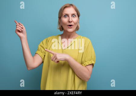Porträt einer überraschten blonden Frau mittleren Alters im gelben T-Shirt auf Studiohintergrund Stockfoto