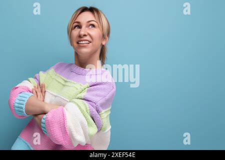 Selbstbewusste blonde junge Frau in einem gestreiften Pullover überkreuzte ihre Arme vor ihr auf blauem Hintergrund Stockfoto