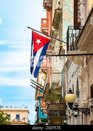 In den historischen Straßen der Altstadt von Havanna zeigt ein flaches Porträt die kubanische Flagge, die an einer alten Fassade im Kolonialstil hängt. Stockfoto