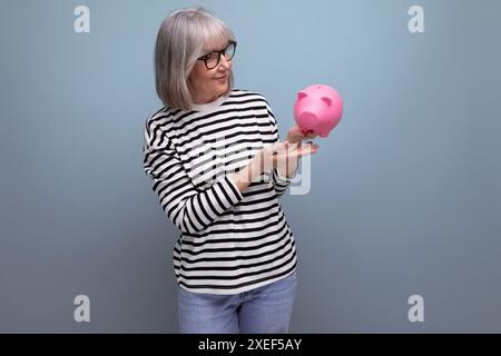 Süße Großmutter, alte Frau 50, die eine Sparkasse mit einer Rente auf einem hellen Hintergrund mit Kopierraum hält Stockfoto