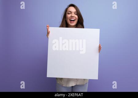 Positive junge brünette Frau, die Werbung auf weißem Blatt zeigt Stockfoto
