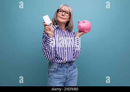 Sozialschutz. Frau mittleren Alters aus den 60er Jahren mit grauem Haar, die eine Schweinebank vor hellem Atelierhintergrund hält Stockfoto