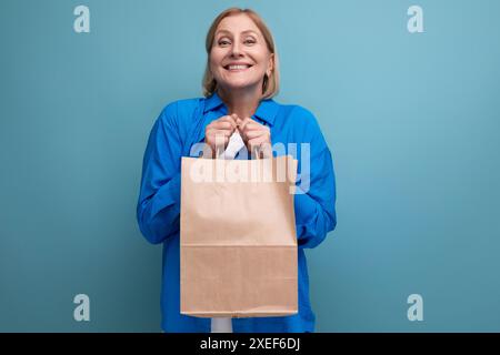 Glückliche Frau mittleren Alters, die umweltfreundliche Handtasche auf blauem Kopierraum-Hintergrund hält Stockfoto