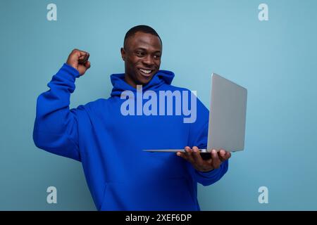 Hübscher, dunkelhäutiger 25 Jahre alter amerikanischer Freelancer in stylischem Hoodie mit Laptop auf Hintergrund und Kopierraum Stockfoto
