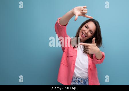 Moderne brünette Frau in rosa Hemd macht Fotos mit Telefon auf Studiohintergrund Stockfoto