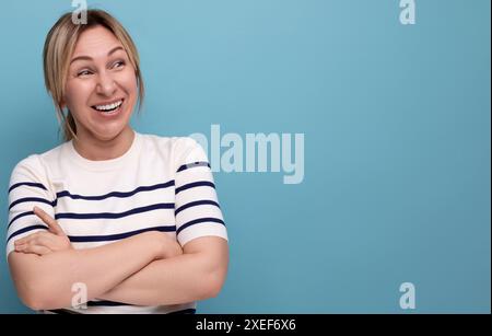 Nahaufnahme Foto einer entzückenden energiegeladenen, glücklichen blonden Millennial-Frau in gestreifter lässiger Bluse auf blauem Hintergrund mit Kopierraum Stockfoto