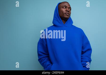 Der stylische coole junge Mann american mit dunkler Haut trägt ein trendiges Sweatshirt mit Kapuze auf Studiohintergrund mit Kopie sp Stockfoto