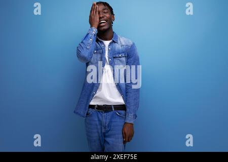 Schöner amerikanischer Mann mit Afro-Locken im lässigen Denim-Outfit auf blauem Hintergrund mit Kopierraum Stockfoto
