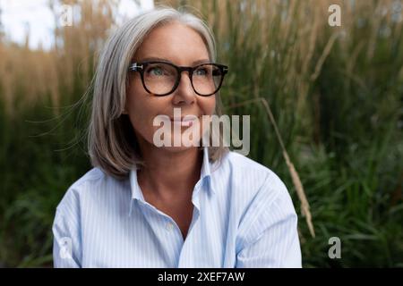 Eine schlanke, süße, grauhaarige Geschäftsfrau, weiße Frau reifer Jahre in einem hellen Hemd, geht auf die Straße Stockfoto