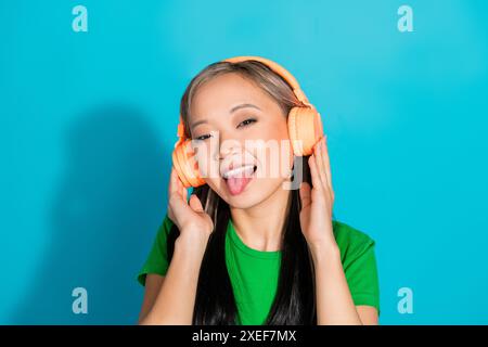 Foto von netten jungen Mädchen Haphone zeigen Zunge tragen grünes T-Shirt isoliert auf blaublauem Hintergrund Stockfoto