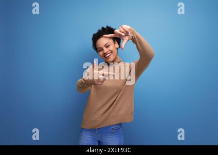 Junge enthusiastische helle lateinische Frau mit lockigen Haaren lächelt auf Hintergrund mit Kopierraum Stockfoto