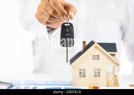 Immobilienmakler mit Hausmodell und Autoschlüssel, Kunde unterzeichnet Vertrag für den Kauf von Haus, Versicherung oder Leihimmobilien. Autoverkäufe Stockfoto