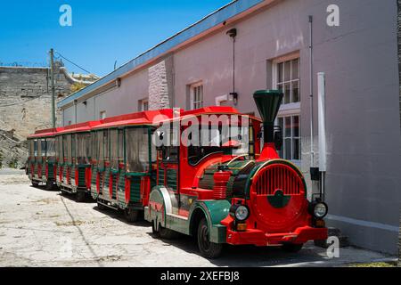 Ein hellroter Zug, der für Touristenfahrten konzipiert ist, parkt in einer Seitenstraße am Naval Dockyard. Stockfoto