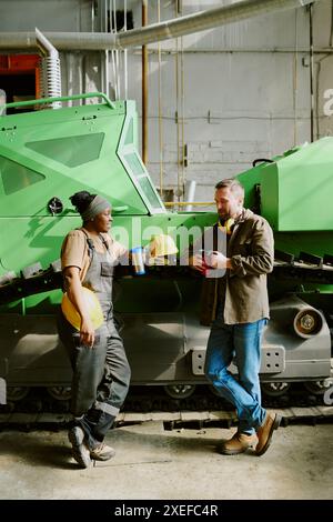 Vertikale Aufnahme junger, ethnisch unterschiedlicher Ingenieure, die während der Mittagspause in der Fabrik plaudern, im Kopierraum Stockfoto