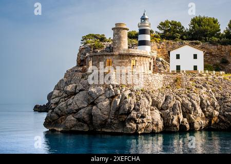 Der Leuchtturm von SA Creu, der in der sanften Morgensonne getaucht ist, überblickt das ruhige Wasser von Port de Sóller, einer alten Leuchtturm-Ruine. Stockfoto