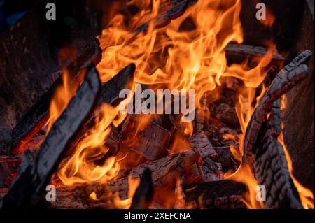 Nahaufnahme eines lebendigen Feuers mit leuchtenden orangen Flammen und verkohlten Baumstämmen, das die Intensität der Hitze einfängt. Stockfoto
