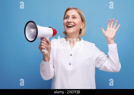 Energische reife Frau mit blondem Haar und Lautsprecher kündigt wichtige Neuigkeiten mit Begeisterung an Stockfoto
