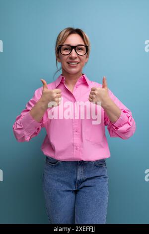 Die junge, selbstbewusste, stilvolle blonde Geschäftsfrau in Brille trägt ein pinkfarbenes Hemd und eine Jeans Stockfoto