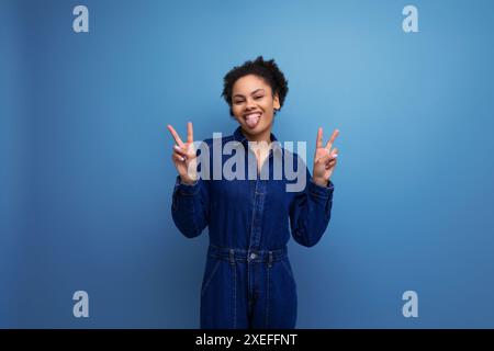 Eine junge brünette lateinfrau mit Afro-Haaren, die in einem Brötchen gefesselt sind, trägt einen blauen, stylischen Denim-Anzug Stockfoto
