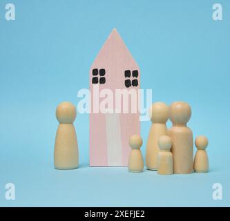 Holzhaus und Miniaturfiguren einer Familie auf blauem Hintergrund. Das Konzept des Verkaufs und Kaufs von Immobilien Stockfoto