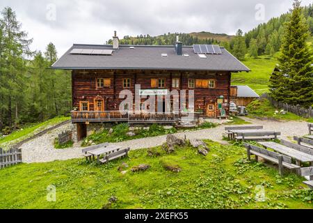 Die Filzmoosalm im Grossartltal, Salzburg, Österreich, liegt auf 1.710 Metern über dem Meeresspiegel vor bewaldeten Hängen. Solarpanele auf dem Dach versorgen die Hütte mit Strom. Holzbänke auf einem Kiesbereich davor laden Besucher zum Ausruhen ein. Stockfoto