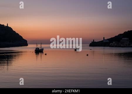 In der Abenddämmerung steigt die Silhouette des Hafeneingangs von Port de Sóller mit einem Fischerboot in ruhigen Gewässern und einem Leuchtturm ab. Stockfoto