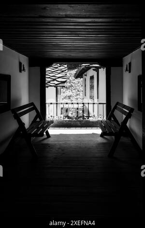 Zwei Holzbänke stehen auf einer Veranda mit Blick auf traditionelle Häuser mit schwarz-weiß gekachelten Dächern Stockfoto