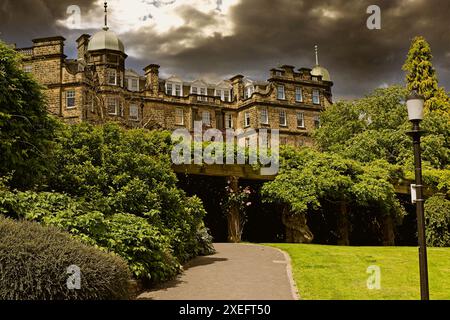 Ein historisches Gebäude mit einem dunklen, bewölkten Himmel im Hintergrund. Das Gebäude ist umgeben von üppigem Grün und einem gut gepflegten Gartenweg, der zum Hotel führt Stockfoto