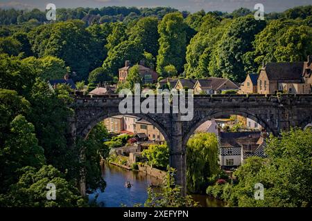 Ein malerischer Blick auf eine historische Steinbrücke über einen Fluss, umgeben von üppigen grünen Bäumen und malerischen Häusern in einer kleinen Stadt. Stockfoto