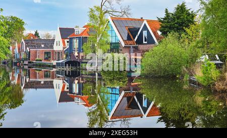 Eine malerische Szene mit einer Reihe von charmanten Häusern, eingebettet an einem ruhigen Gewässer, reflektiert den klaren blauen Himmel und Stockfoto