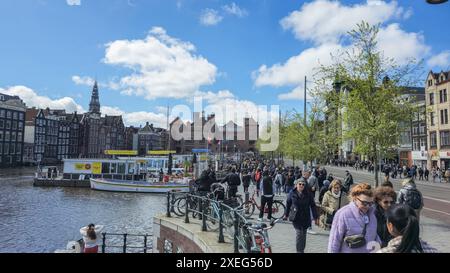 Amsterdam Niederlande 21. April 2024 schlendern eine vielfältige Gruppe von Menschen entlang einer charmanten Straße neben einem friedlichen Fluss und bewundern die Landschaft und chatti Stockfoto