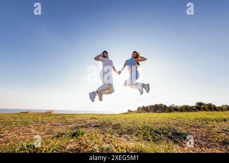 Zwei multiethnische Freunde in lässiger Kleidung und panamahüten springen und lachen draußen. Junge, fröhliche Frauen verschiedener Art Stockfoto