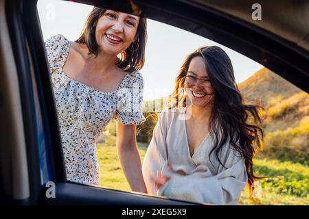 Junge Frauen verschiedener Rassen lachen und haben Spaß während der Reise. Ansicht vom Fenster des Fahrzeugs. Stockfoto