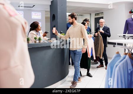 Black Friday Shopping. Freundliche afroamerikanische Frau Bekleidungsgeschäft Kassierer für männliche Kunden, Verkäuferin steht hinter der Kasse und scannt den mobilen Aktionscode vom Mobiltelefon Stockfoto