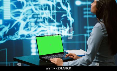 Startup-Mitarbeiter schauen sich Diagramme an und nutzen KI-Software auf einem Green Screen-Laptop, um datenbasierte Entscheidungen zu treffen. Indische Frau, die innovative künstliche Intelligenz-Lösungen für Unternehmen entwickelt, Kamera A Stockfoto