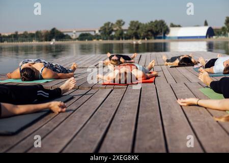 Yoga-Kurs am Morgen mit einem Lehrer am Yachthafen in der Stadt. Junge gesunde Frauen liegen in Shawasan auf Matten in der Nähe des Flusses. Stockfoto