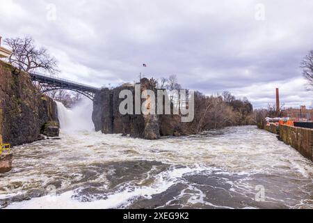 Malerische Aussicht auf den Wasserfall in New Jersey, mit einem mächtigen Wasserfluss, der über Klippen mit Brücke und amerikanischer Flagge im Hintergrund fließt. Stockfoto