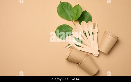 Pappbecher, Holzlöffel und Gabeln auf beigefarbenem Hintergrund Stockfoto