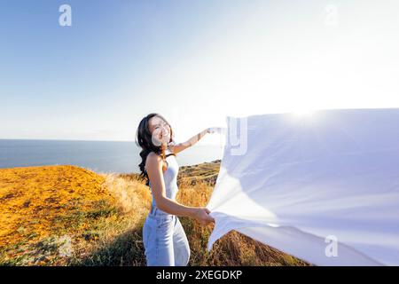 Eine attraktive asiatische Frau lacht und hält draußen ein offenes Laken. Eine charmante Koreanerin genießt die Natur. Stockfoto