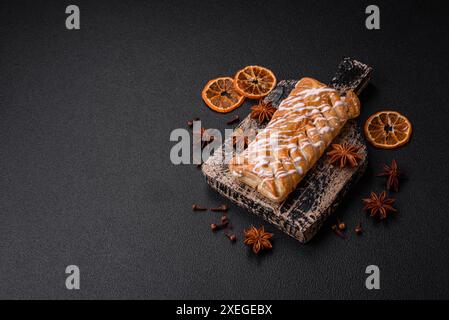 Köstliches knuspriges geflochtenes Brötchen mit Rosinen innen und weißer Zuckerglasur außen auf dunklem Betonhintergrund Stockfoto