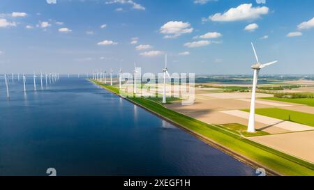 Ein ruhiger, großer Wasserkörper, umgeben von Windmühlen, die aktiv Strom mit der Kraft des Windes erzeugen Stockfoto