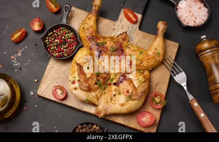 Ganze gebratene Hühnchen mit Gewürzen auf einem Holzbrett auf einem schwarzen Tisch Stockfoto